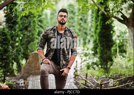 Awesome beautiful tall ararbian beard macho man in glasses and military jacket posed outdoor. Stock Photo