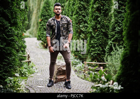 Awesome beautiful tall ararbian beard macho man in glasses and military jacket posed outdoor. Stock Photo