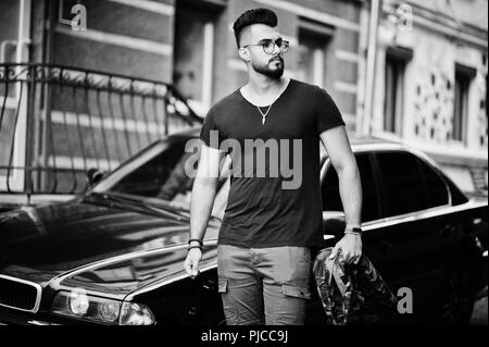 Awesome beautiful tall ararbian beard macho man in glasses and black t-shirt walking against business car. Stock Photo