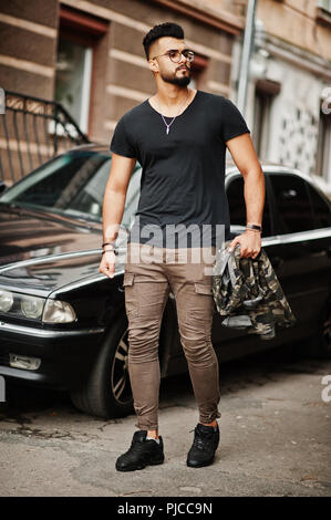 Awesome beautiful tall ararbian beard macho man in glasses and black t-shirt walking against business car. Stock Photo