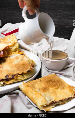 Delicious puff pastry apple, cherry pie on white tablecloth and cup of coffee with cream jug. Stock Photo