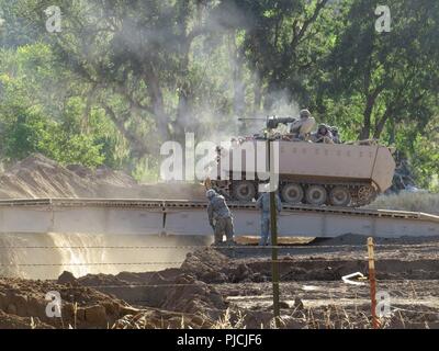 U.S. Army Reserve engineers assault with an M2 .50 caliber machine gun while crossing a bridge in their M113 Armored Personnel Carrier during Combat Support Training Exercise (CSTX) 98-18-01 at Fort Hunter Liggett, Calif., on July 22, 2018. The engineers opened two breach lanes across an enemy trench while suppressing enemy soldiers with volleys of machine gun fire. CSTX 91-18-01 ensures America’s Army Reserve units are trained to deploy bringing capable, combat-ready, and lethal firepower in support of the Army and our joint partners anywhere in the world. Stock Photo