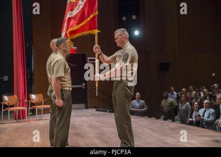 U.S. Marine Corps Sgt. Maj. Michael Hensley, right, base sergeant major, Marine Corps Base Quantico (MCBQ), passes the U.S. Marine Corps ensign to Col. Joseph Murray, outgoing base commander, during a change of command ceremony at Warner Auditorium, Quantico, Va., July 13, 2018. During the ceremony, Murray relinquished command to Col. William C. Bentley, incoming base commander. Stock Photo