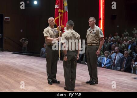 U.S. Marine Corps Col. William C. Bentley, left, base commander, Marine Corps Base Quantico (MCBQ), receives the U.S. Marine Corps ensign from Col. Joseph Murray, center, outgoing base commander, MCBQ, during a change of command ceremony at Warner Auditorium, Quantico, Va., July 13, 2018. During the ceremony, Murray relinquished command to Bentley. Stock Photo