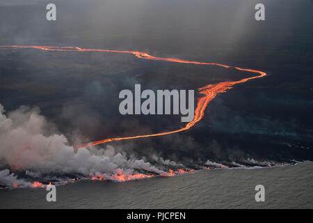 lava erupted from fissure 8 of Kilauea Volcano east rift zone near Pahoa, Hawaii flows as a glowing river through Kapoho to enter the Pacific Ocean. Stock Photo