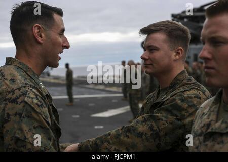 PACIFIC OCEAN - U.S. Marine Sgt. Jonathan Ritter III, a rifleman with Lima Company, Battalion Landing Team 3/1, 13th Marine Expeditionary Unit (MEU), is congratulated by Capt. Stephen Greenberg, his commanding officer, after being awarded a Navy and Marine Corps Achievement Medal aboard the Wasp-class amphibious assault ship USS Essex (LHD 2) during a regularly scheduled deployment of the Essex Amphibious Ready Group (ARG) and the 13th MEU, July 14, 2018. The Essex ARG/MEU team is a strong, flexible, responsive and consistent force capable of maneuver warfare across all domains; it is equipped Stock Photo