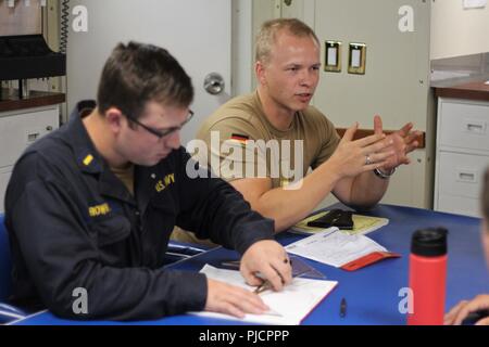 GULF OF OMAN (July 27, 2018) Lt. j.g. Simonas Vollmer, right, of the German navy, trains junior officers on the fundamentals of maneuvering boards aboard the guided-missile destroyer USS The Sullivans (DDG 68). The Sullivans is deployed to the U.S. 5th Fleet area of operations in support of naval operations to ensure maritime stability and security in the Central region, connecting the Mediterranean and the Pacific through the western Indian Ocean and three strategic choke points. Stock Photo