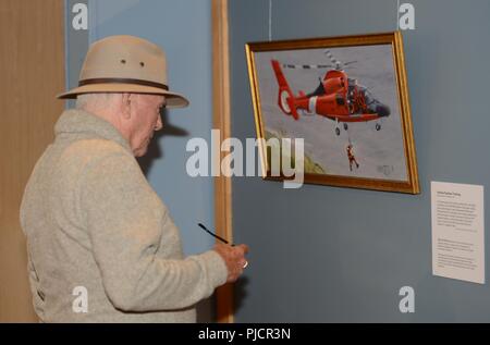 A visitor to the Coos History Museum looks at a piece of art from the Coast Guard Art Program, during the opening night of the gallery showcase in Coos Bay, Ore., July 19, 2018.    Through displays at museums, libraries and patriotic events, Coast Guard art tells the story of the service's missions, heroes and history to the public.    U.S. Coast Guard Stock Photo