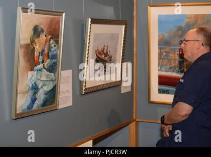 Lt. Cmdr. William Stewart, chaplain Coast Guard 13th District, views paintings from the Coast Guard Art Program gallery at the Coos History Museum during the opening night of the art showcase in Coos Bay, Ore., July 19, 2018.    Through displays at museums, libraries and patriotic events, Coast Guard art tells the story of the service's missions, heroes and history to the public.    U.S. Coast Guard Stock Photo