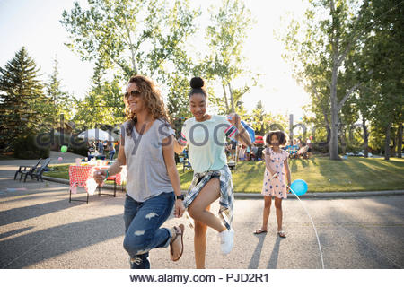 Mother and daughters jump roping at summer neighborhood block party in street