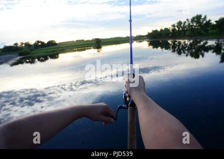 Airman John Ennis, a 28th Bomb Wing Public Affairs broadcast journalist, reels his rod at Gateway Lake on Ellsworth Air Force Base, S.D., July 12, 2018. Some fish species are allowed to be entered in South Dakota fishing records. Stock Photo