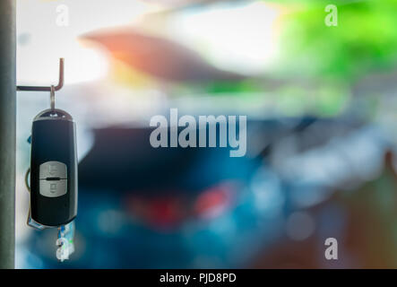 Black and silver car key hang on metal pole on blurred background of luxury blue SUV car. Car rental and automobile insurance. Auto leasing and sale.  Stock Photo