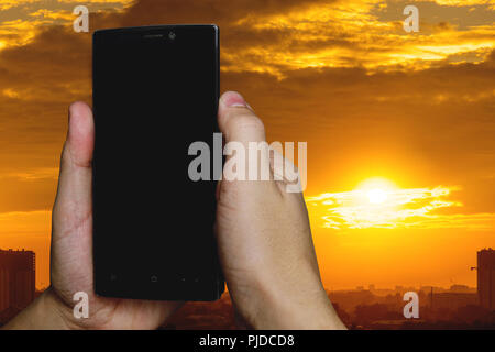 man using a touch screen smart phone hands in sunset sky on blurred urban city as background, vintage colors Stock Photo