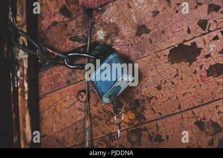 Lock on the door of an old wood house, village style. the key into the old metal lock on the background of the Stroy doors in shabby paint. Locked doo Stock Photo