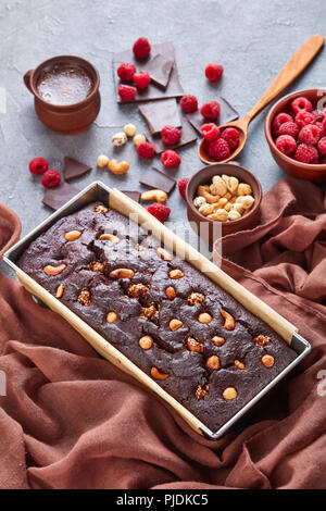 close-up of chocolate buckwheat pound cake with nuts and raspberries in a metal baking mold on a concrete table with cup of coffee, view from above, v Stock Photo