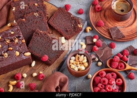 close-up of chocolate buckwheat pound cake with nuts and raspberries cut in slices on a wooden board on a concrete table with cup of coffee and brown  Stock Photo