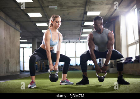 Trainer and female client exercise with kettlebells in gym Stock Photo