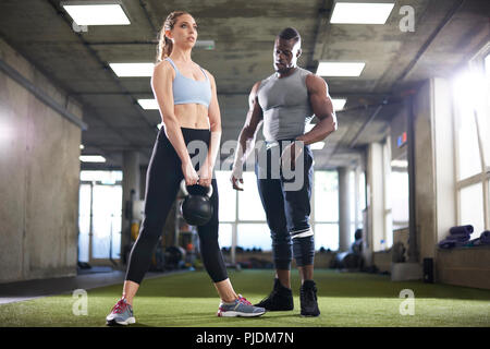 Trainer watching female client exercise with kettlebell in gym Stock Photo