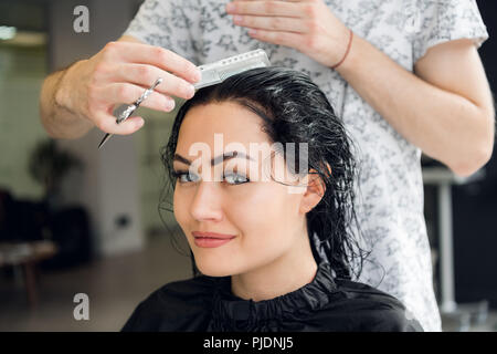 Hairdresser cutting woman's hair in salon, smiling, front view, close-up, portrait Stock Photo