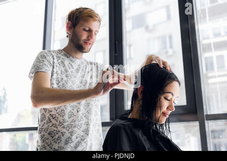 Hairdresser cutting client's hair in salon with scissors closeup. Using a comb Stock Photo