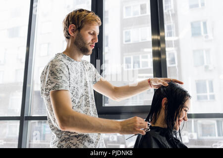 The hairdresser does a haircut with scissors of hair to a young girl in a beauty salon. Stock Photo