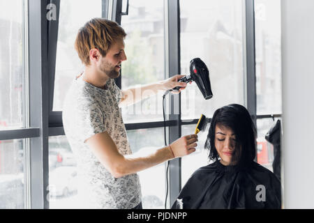 Young woman getting her hair dressed in hair salon by a handsome hairdresser hairstylist Stock Photo