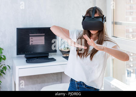 Smiling positive woman wearing virtual reality goggles headset, vr box. Connection, technology, new generation, progress concept. Girl trying to touch Stock Photo