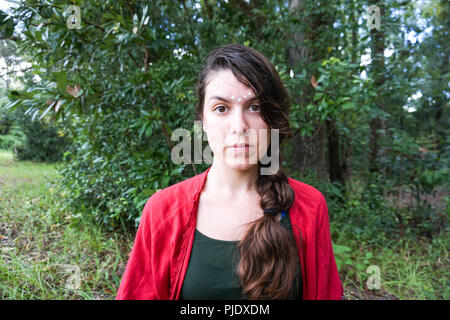 Young hippie beautiful brunette woman with long braid hair with white tribal makeup next to a tree Stock Photo