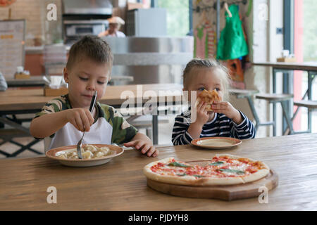 kids eat pizza and meat dumplings at cafe. children eating unhealthy food indoors. Siblings in the cafe, family holiday concept. Stock Photo