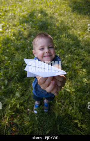 Paper airplane in kid hands close-up. Toddler boy 4 years old holding origami plane in park or garden in shadoow in summer sunny day. Hobby, leisure,  Stock Photo