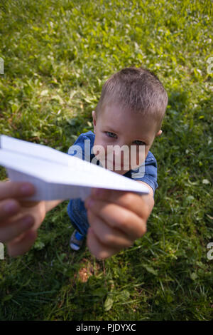 Cute caucasian child playing paper airplane in the park outdoors in summer sunny day Stock Photo