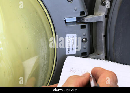 Writing down the manufacturer's serial and model numbers on the inside of a washing machine door Stock Photo