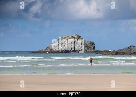 A holidaymaker standing in the sea at Crantock Beach looking out to The Goose a small rocky uninhabited island off East pentire Headland in Newquay Co Stock Photo