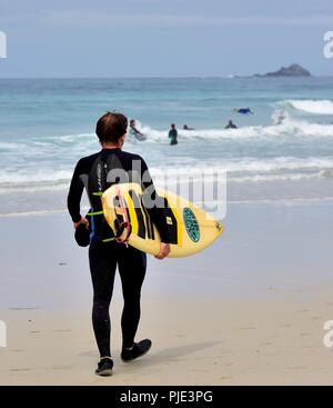 A man carrying a surfboard walking towards the sea,Sennen Cove,Cornwall,England,UK Stock Photo