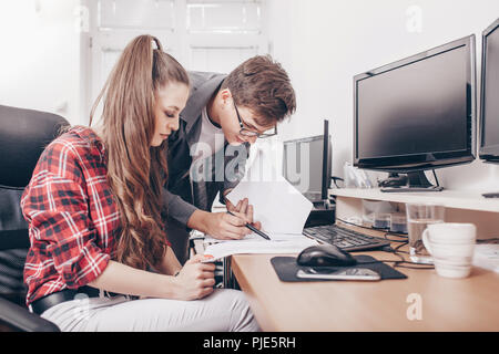 Young smart man pointing with pen on paper showing information to young female woman  colleague working in team. Stock Photo