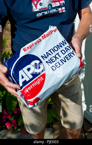 Close up of person man courier delivering APC overnight express mail parcel internet shopping delivery England UK United Kingdom GB Great Britain Stock Photo