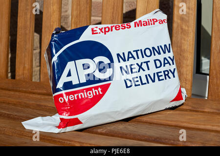 Close up of APC overnight express mail parcel package delivery left on bench outside house England UK United Kingdom GB Great Britain Stock Photo