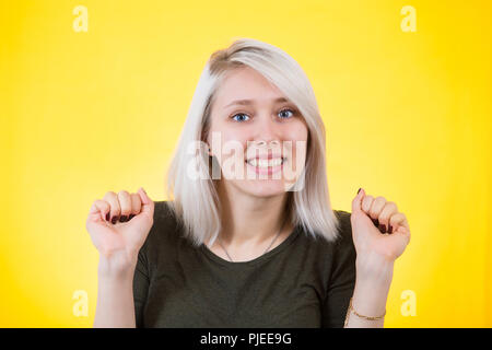 Young woman clenching her fists tight for encouragement, success concept isolated over yellow bakground. Expression of hope and support. Stock Photo