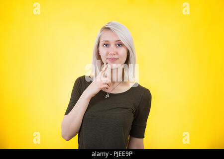 Close up portrait of pretty confident thoughtful girl, holding hand near the face under chin, looking seriously to camera, standing over colorful yell Stock Photo