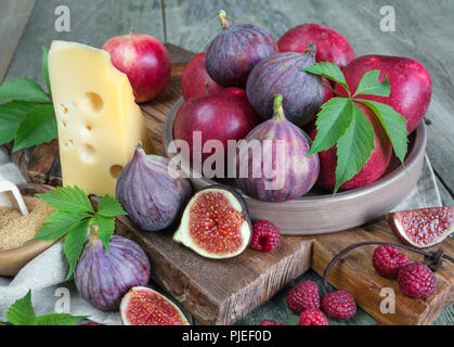 Ripe figs, red raspberry and apples, cane sugar and cheese are on old cutting board as well as green leaves lie on the old wooden table Stock Photo