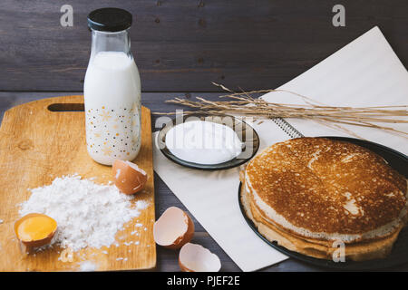 fresh, hot pancakes in a frying pan, eggs, milk, flour on a wooden table Stock Photo