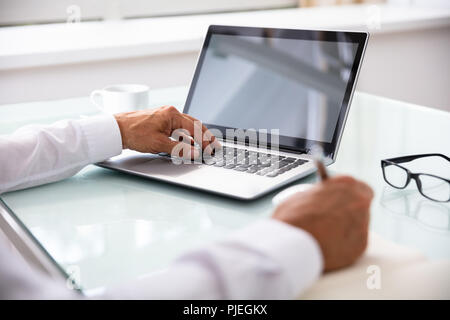 Businessman's Hand Using Laptop While Writing Schedule In Diary Stock Photo