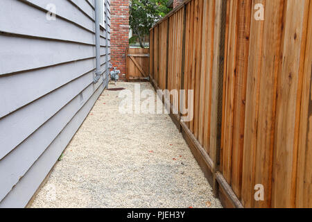 Long narrow side yard, new wood fence on the right with house on the left, home paint chipping and peeling. Meter by brick chimney exterior, fence to  Stock Photo