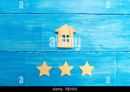 Wooden house and three stars on a blue background. Rating of houses and private property. Buying and selling, renting apartments. The level of the res Stock Photo