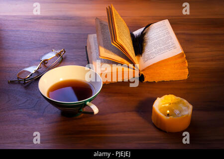 An open book on the table. A gloomy burning candle. Stock Photo