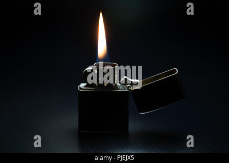 Lighter burning in darkness. Metallic lighter with red hot flame isolated on black background. Stock Photo