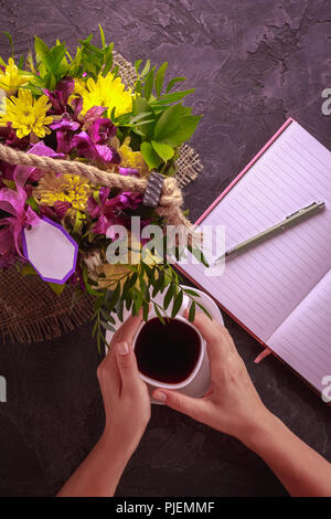 Female hands with a cup of tea top view flowers in a bouquet and a notebook for writing with a pen Stock Photo
