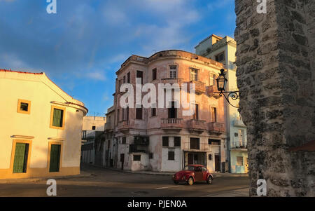 Red retro car moving on the bright streets of Havana, dilapidated facades of buildings with elements of architectural decor, cultural heritage of Spai Stock Photo