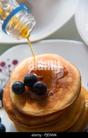 Maple syrup spilling on fresh homemade pancakes with blueberries, sweet tasty breakfast meal detail Stock Photo