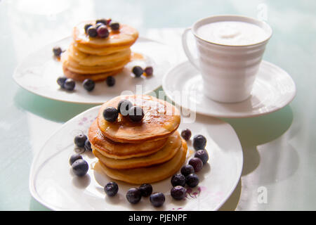 Breakfast pancakes on the stylish plate served with fresh blueberries and topped with original maple syrup, next cup of creamy white coffee Stock Photo
